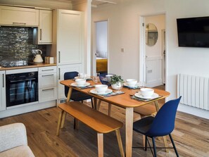 A modern kitchen with white cabinets, a black oven, and a wooden dining table set with white plates and blue chairs.