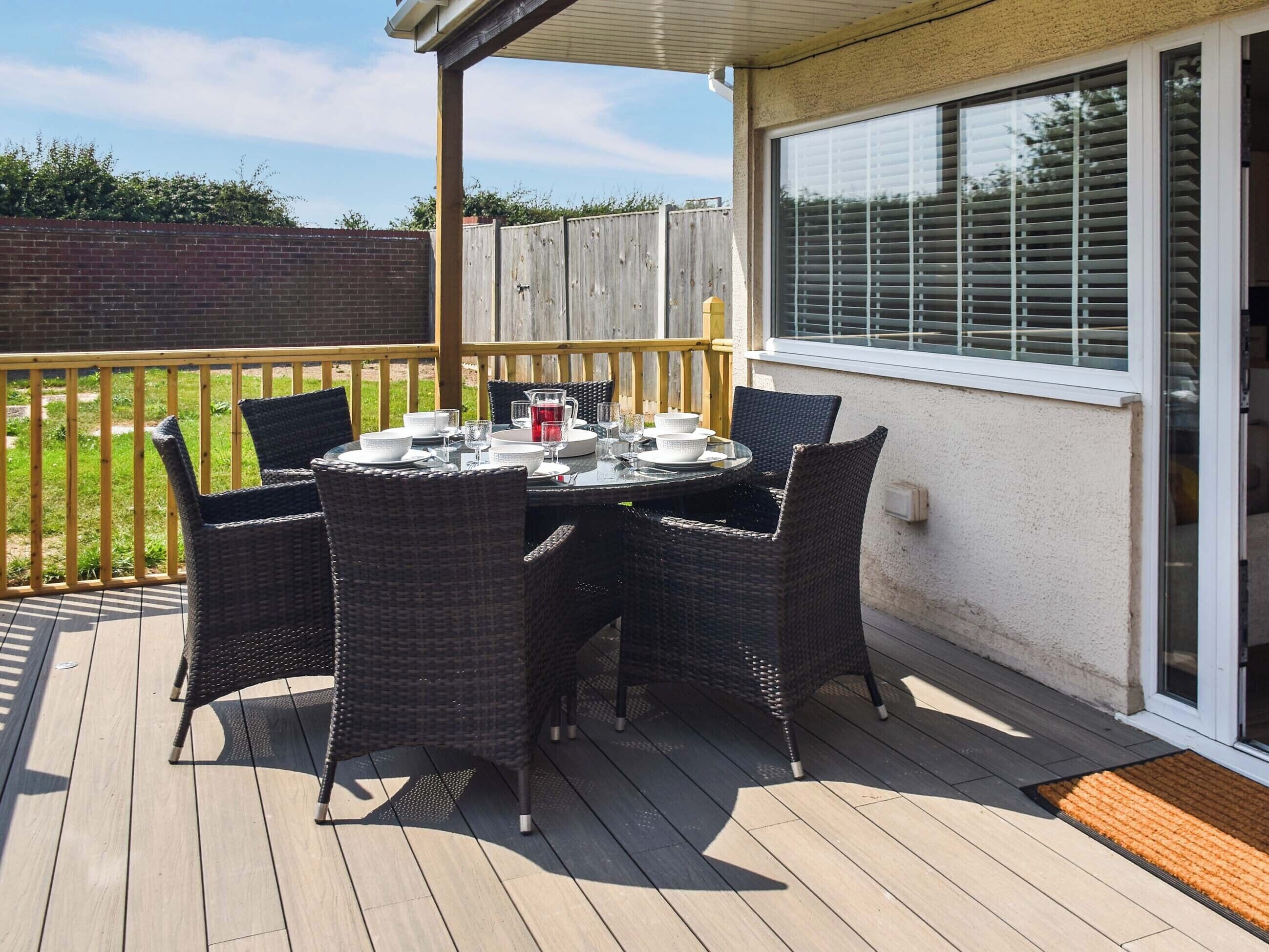 A covered outdoor patio with a table set for four, surrounded by wicker chairs.