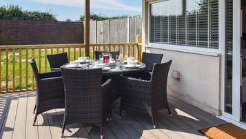 A covered outdoor patio with a table set for four, surrounded by wicker chairs.