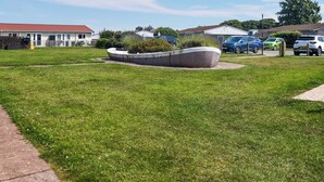 Un espacio con césped, un macetero de concreto circular, un sendero pavimentado y coches estacionados al fondo.