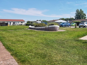 A grassy area with a circular concrete planter, a paved walkway, and parked cars in the background.