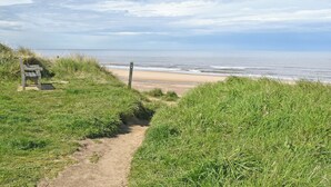 Un camino costero que lleva a una playa, con un banco y una señal.