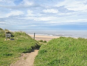 A coastal path leading to a beach with a bench and a signpost.