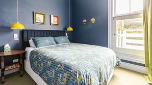 Een slaapkamer met een bed, twee nachtkastjes, een raam met gordijnen en decoraties aan de muur.