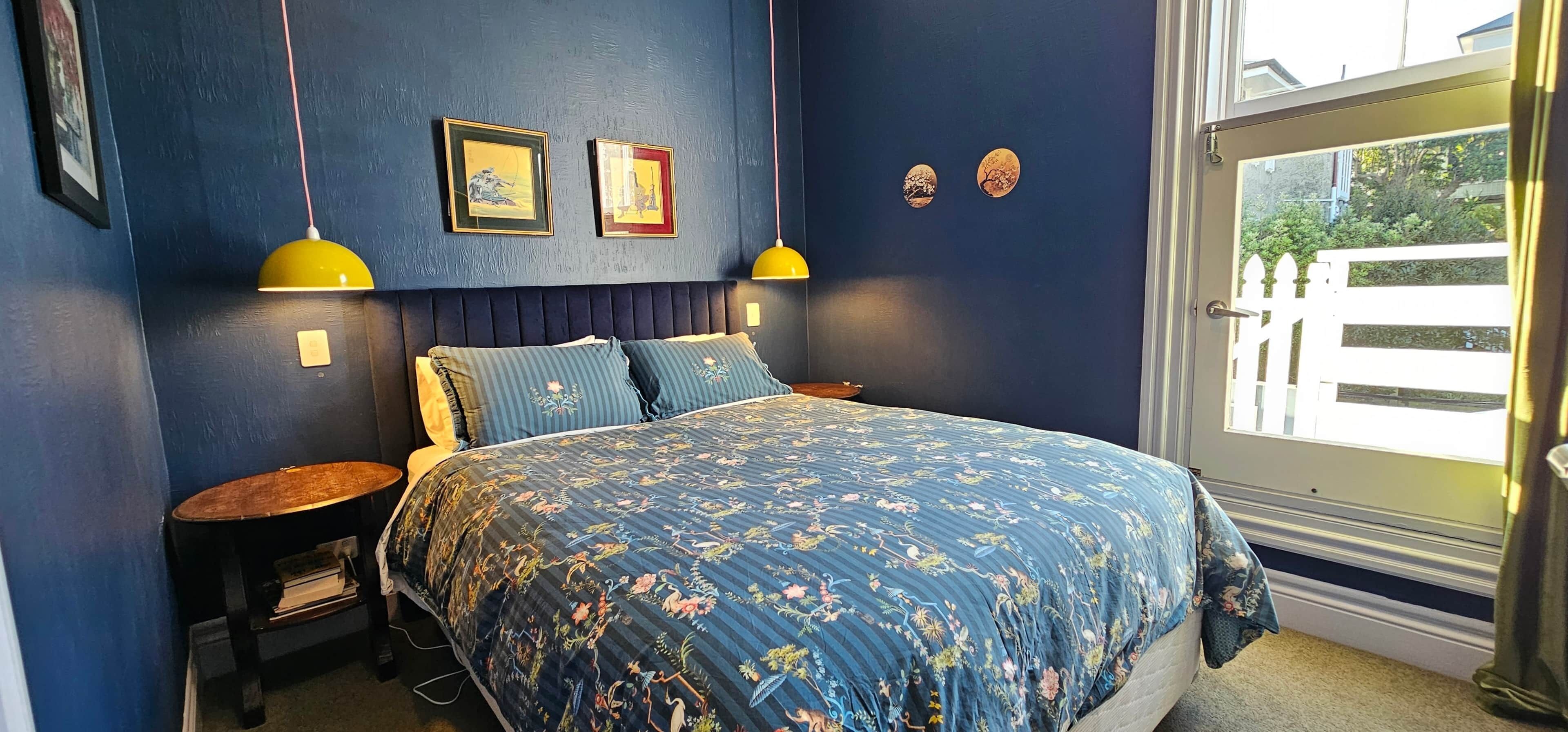 A bedroom with a bed, two nightstands, a window with a view, and wall art.