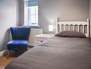 Ein Schlafzimmer mit Bett, Stuhl, Nachttisch, Lampe und Fenster.