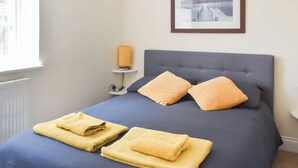 Ein ordentlich bezogenes Bett mit zwei Kissen, einer Nachttischlampe und einem gerahmten Bild an der Wand.