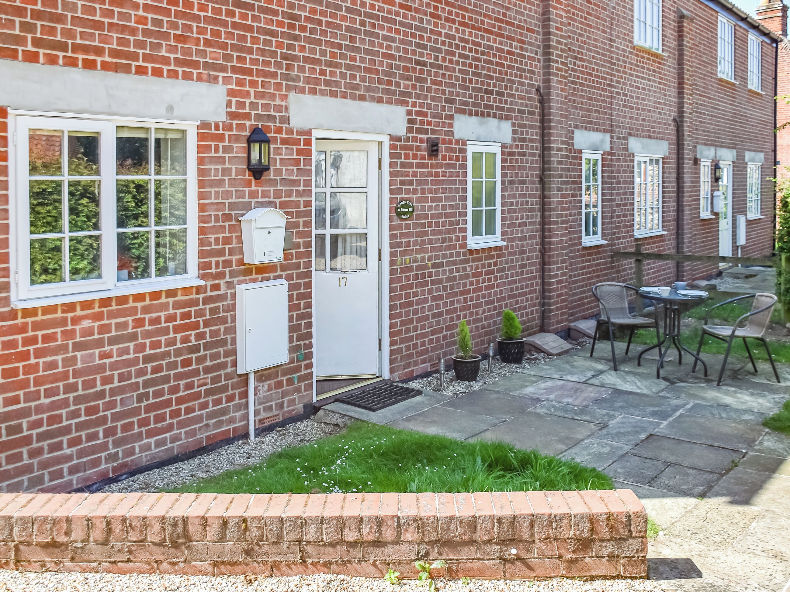 A red brick house with white-framed windows, a white door, and a small outdoor seating area with chairs and a table.