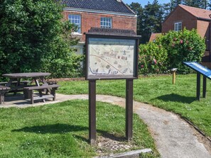Ein Wegweiser in einem Park mit Picknicktischen und einem Backsteinhaus im Hintergrund.