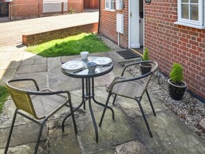 Eine Terrasse mit einem runden Tisch, zwei Korbstühlen und einem Blumentopf.