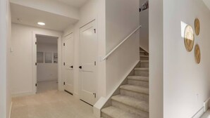 A hallway with carpeted floors, white doors, a staircase, and wall-mounted woven decorations. - Pavilion Lakefront Luxe 3 Bdrm near Lake! (Chestermere)