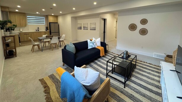A modern living room with a sofa, coffee table, and dining area. - Pavilion Lakefront Luxe 3 Bdrm near Lake! (Chestermere)