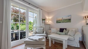 Una habitación acogedora con un sofá blanco, una mesita y una silla con cojín.