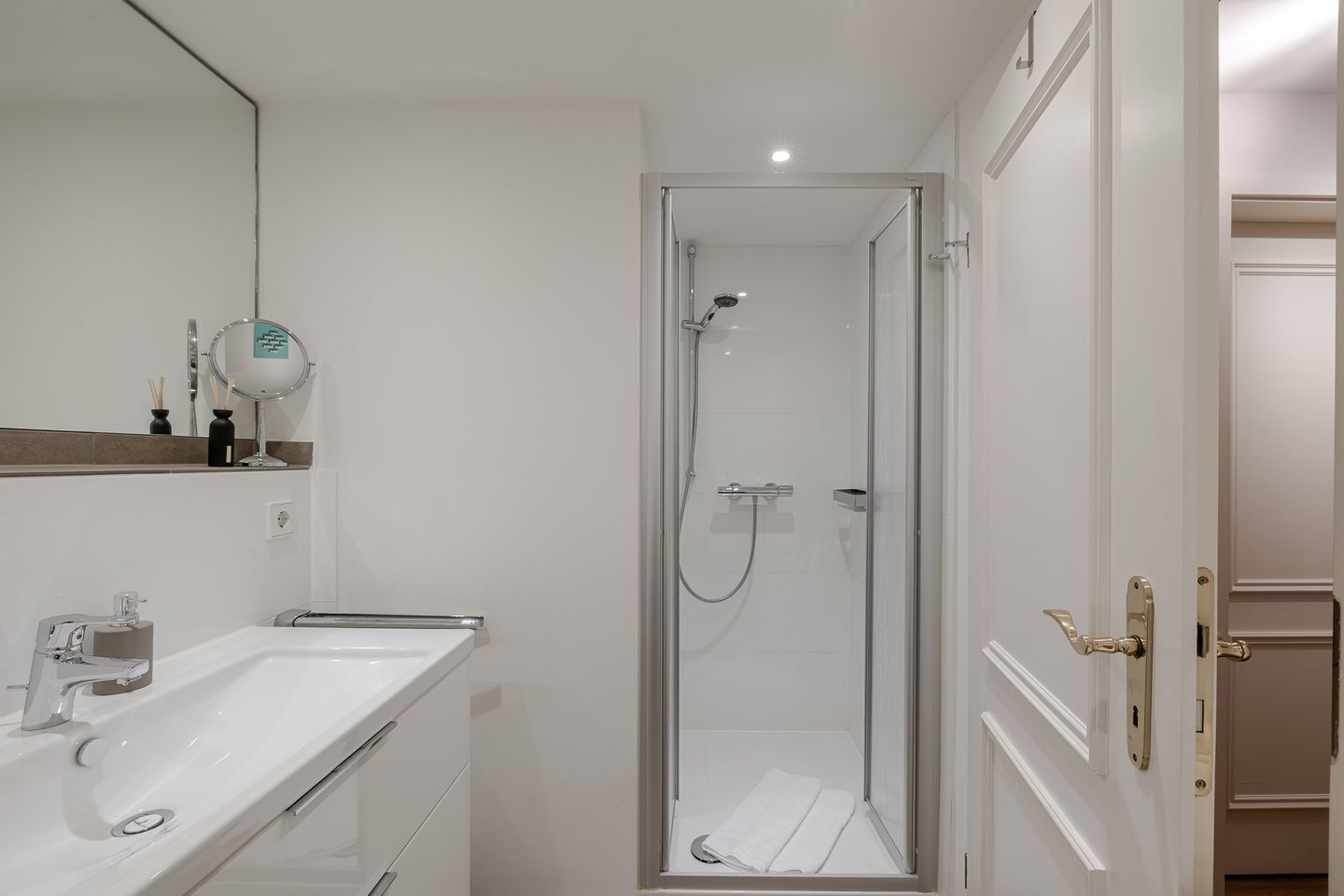 A modern bathroom with a glass-enclosed shower, a white sink, and a mirror above it.
