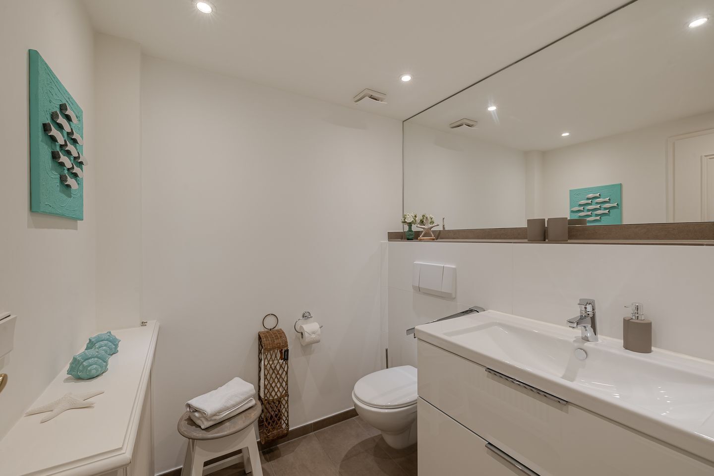 A modern bathroom with a white sink, mirror, and toilet.