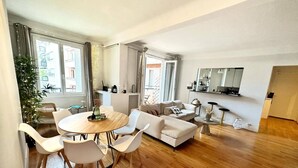 A modern living room with a dining area, white furniture, and large windows. - Charming Parisian Retreat with Eiffel Tower Views (Paris)