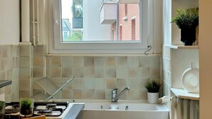 A compact kitchen with a window, a sink, cabinets, and a countertop. - Charming Parisian Retreat with Eiffel Tower Views (Paris)