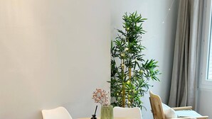 A round wooden table with white chairs, a small vase with flowers, and a tall green plant in the corner. - Charming Parisian Retreat with Eiffel Tower Views (Paris)