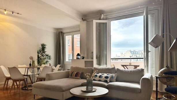 A modern living room with a sectional sofa, a round coffee table, and a dining area with chairs and a table. - Charming Parisian Retreat with Eiffel Tower Views (Paris)