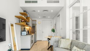 A modern kitchen with wooden shelves, a dining area with a table and chairs, and a living room with a sofa and a coffee table. - Bloomfields 1BR - Golf Ville - DXB Hills (Dubai)
