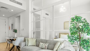 A modern living room with a grey sofa, a dining table, and a potted plant. - Bloomfields 1BR - Golf Ville - DXB Hills (Dubai)