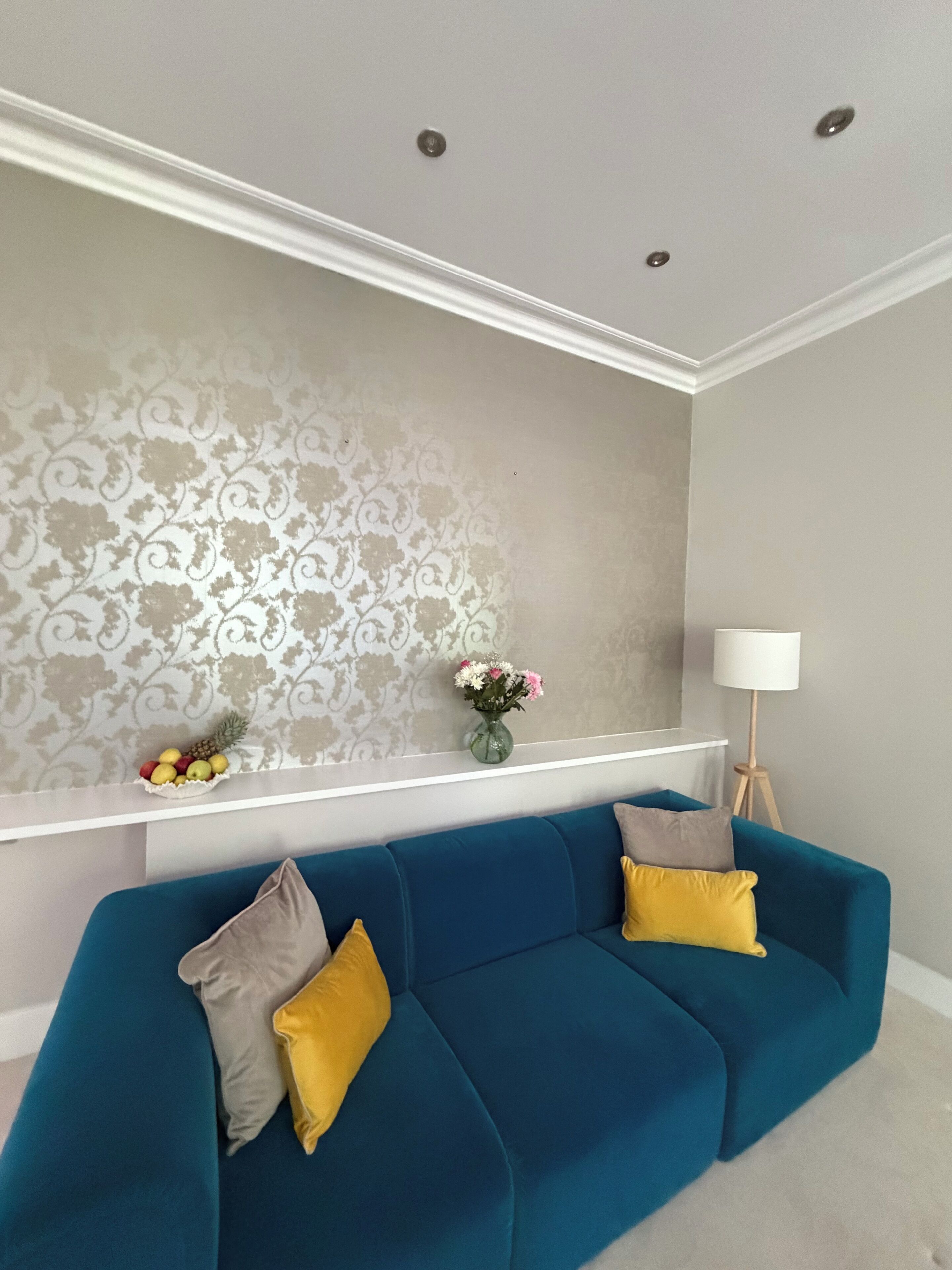 Sala de estar com um sofá azul, uma mesa de console branca, um vaso com flores e um abajur.