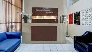 Ein Empfangstresen mit dem Schild 'Kupang Gunung Residence', eine blaue Couch und eine Wand mit Muster.