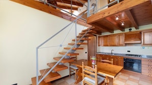 Une cuisine avec des meubles en bois, une table à manger et un escalier doté de rampes en métal.