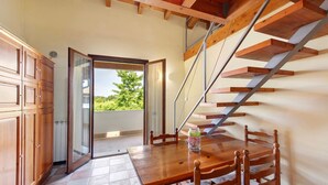 Une table à manger en bois avec des chaises, une porte vitrée donnant sur l’extérieur et un escalier en bois.