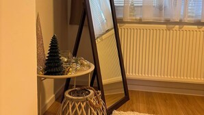 A room with a standing mirror, a small round table with decorative items, a woven basket, and a radiator. - Feel Sarajevo Apartments 2 + Free parking (Sarajevo)