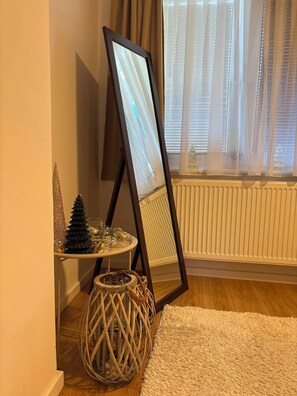 Ein Zimmer mit einem Stehspiegel, einem kleinen runden Tisch mit Dekoration, einem gewebten Korb und einer Heizung.