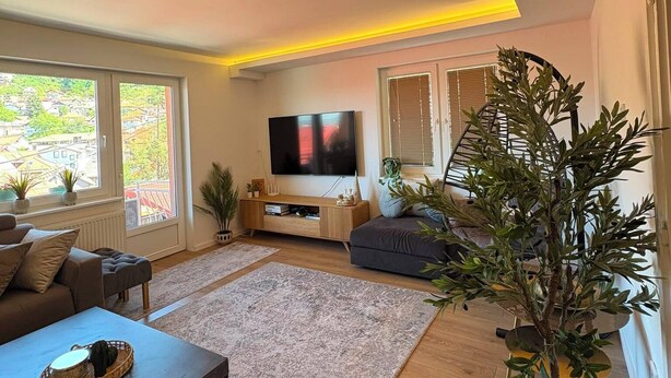 A modern living room with a flat-screen TV, a sofa, a coffee table, and a potted plant. - Feel Sarajevo Apartments 2 + Free parking (Sarajevo)