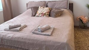 A neatly made bed with a floral pillow, two towels, and a vase with flowers on the side. - Feel Sarajevo Apartments 2 + Free parking (Sarajevo)