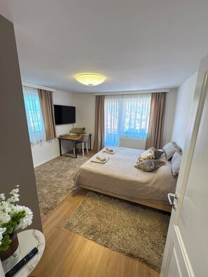 A hotel room with a bed, a desk, a TV, and a window with curtains. - Feel Sarajevo Apartments 2 + Free parking (Sarajevo)