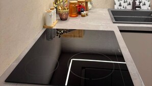 A modern kitchen with a black induction cooktop, a wooden cutting board, a stainless steel sink, and a patterned backsplash. - Feel Sarajevo Apartments 2 + Free parking (Sarajevo)