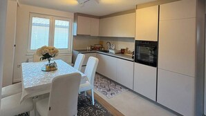 A compact kitchen with white cabinetry, a dining table with chairs, and a small island with a vase of flowers. - Feel Sarajevo Apartments 2 + Free parking (Sarajevo)