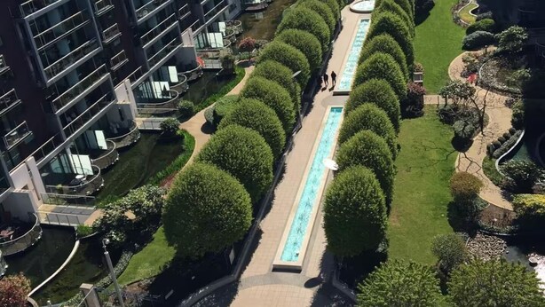 Um edifício residencial alto com um pátio central que apresenta uma piscina e árvores bem aparadas.