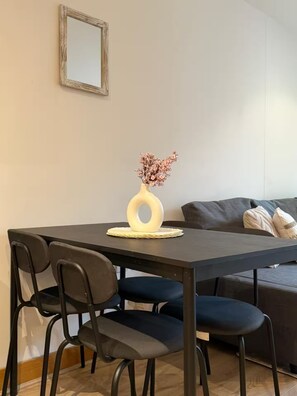 Ein Essbereich mit Tisch, Stühlen, einer Blumenvase und einer Couch im Hintergrund.