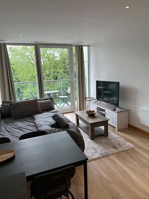 Ein modernes Wohnzimmer mit einer Couch, einem Couchtisch, einem Fernseher und einem Balkon mit Sitzmöbeln.