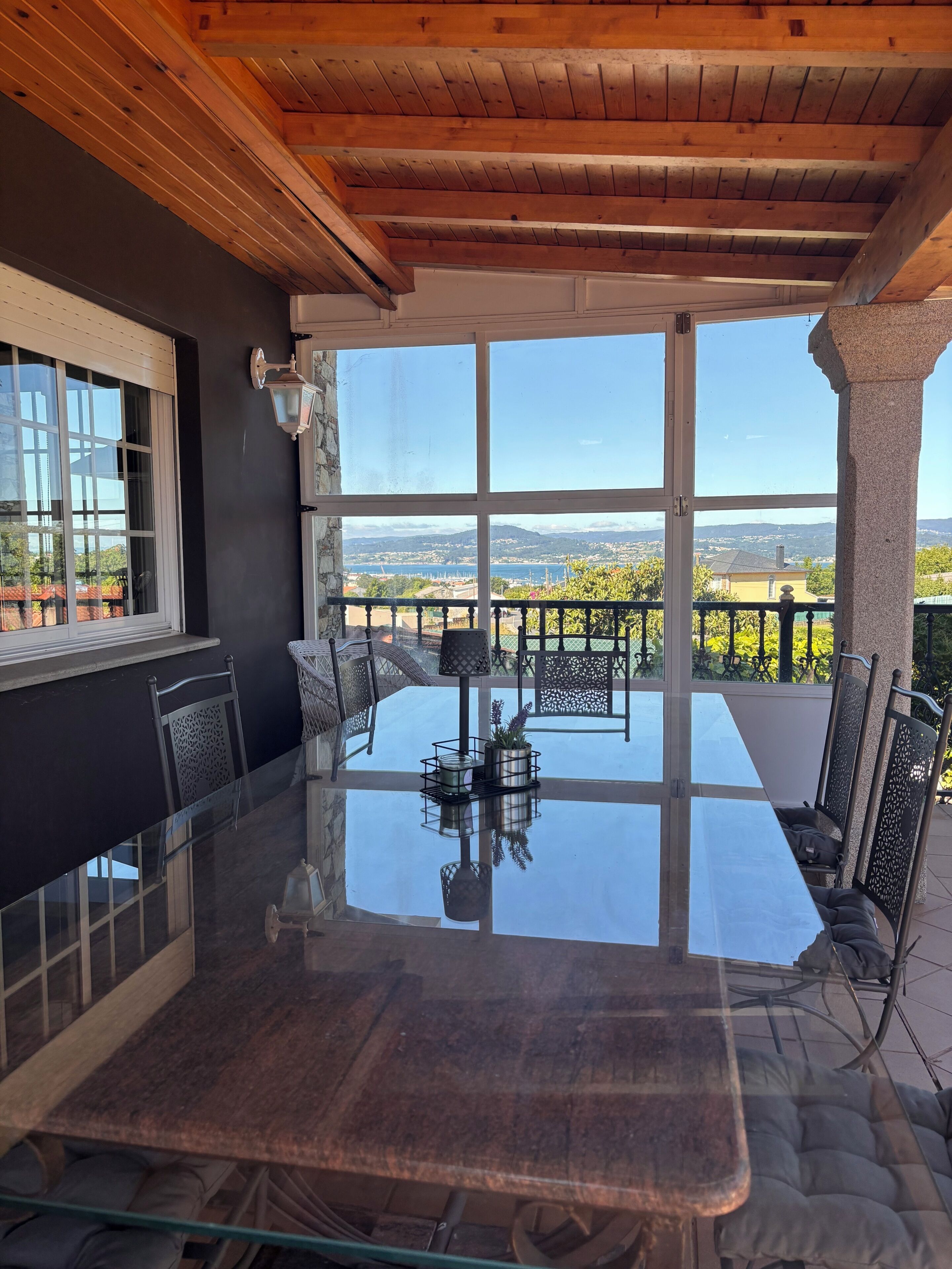 A glass-top dining table with chairs, a view of the landscape, and a stone pillar.