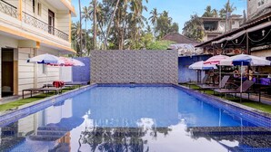 A swimming pool with tiled edges, surrounded by lounge chairs and umbrellas, with a stone wall in the background. - Super Deluxe Room Kris Resort (Calangute)
