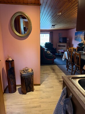 Ein gemütliches Zimmer mit Holzboden, einem runden Spiegel, einem Esstisch mit Stühlen, einem Fernseher und einem Fenster mit Blick.