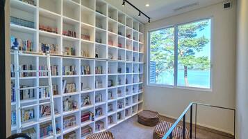 A spacious room with a large bookshelf filled with books, a window with a view of trees, and a staircase with a railing.