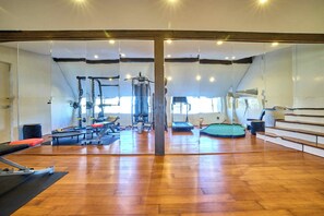 Un gimnasio con equipamiento de ejercicio, suelos de madera y ventanas amplias.