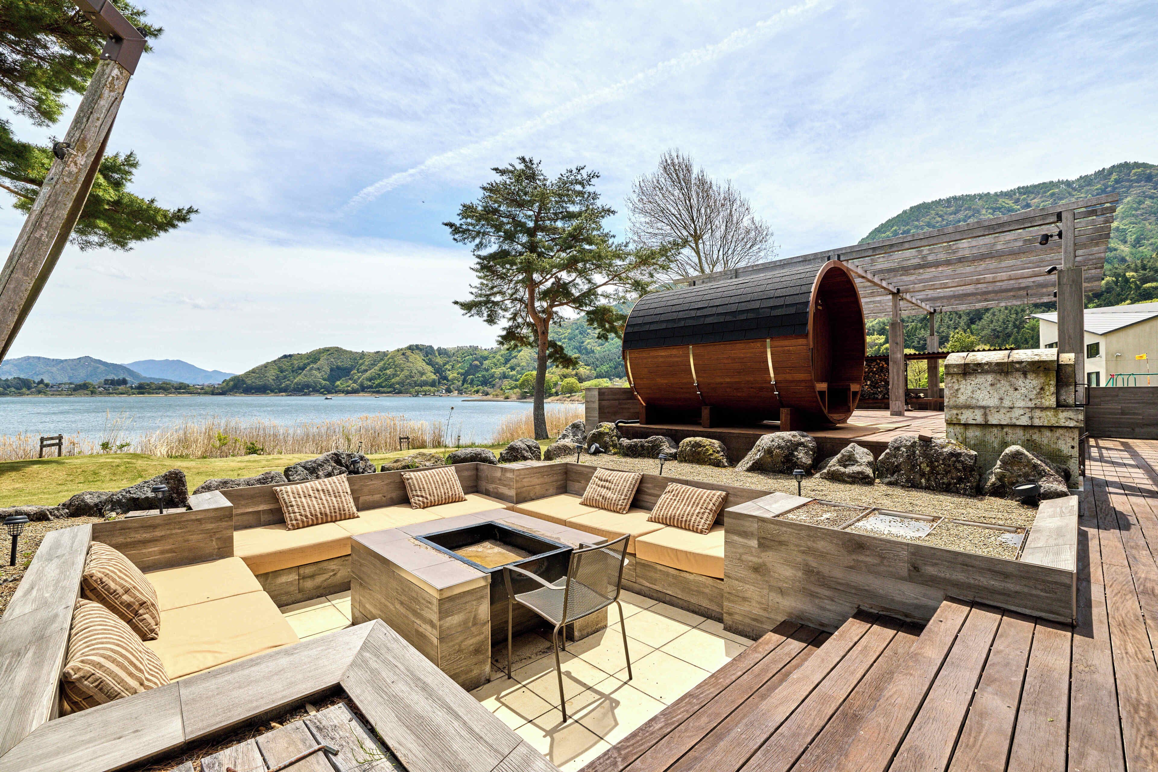 A wooden deck with a built-in seating area and a fire pit, overlooking a lake and hills.