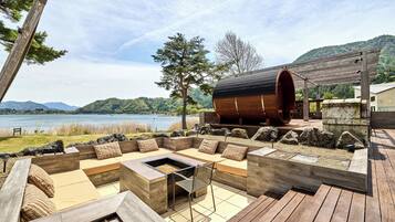 A wooden deck with a built-in seating area and a fire pit, overlooking a lake and hills.