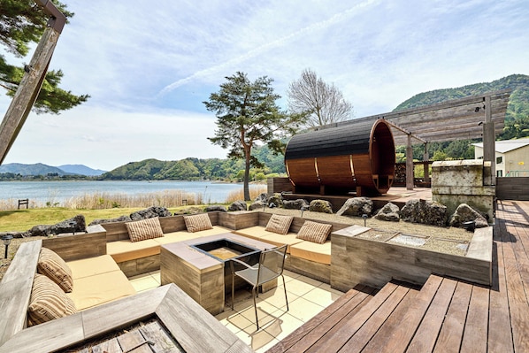 Una terraza de madera con zona de estar integrada y un hogar para fuego, con vistas a un lago y colinas.