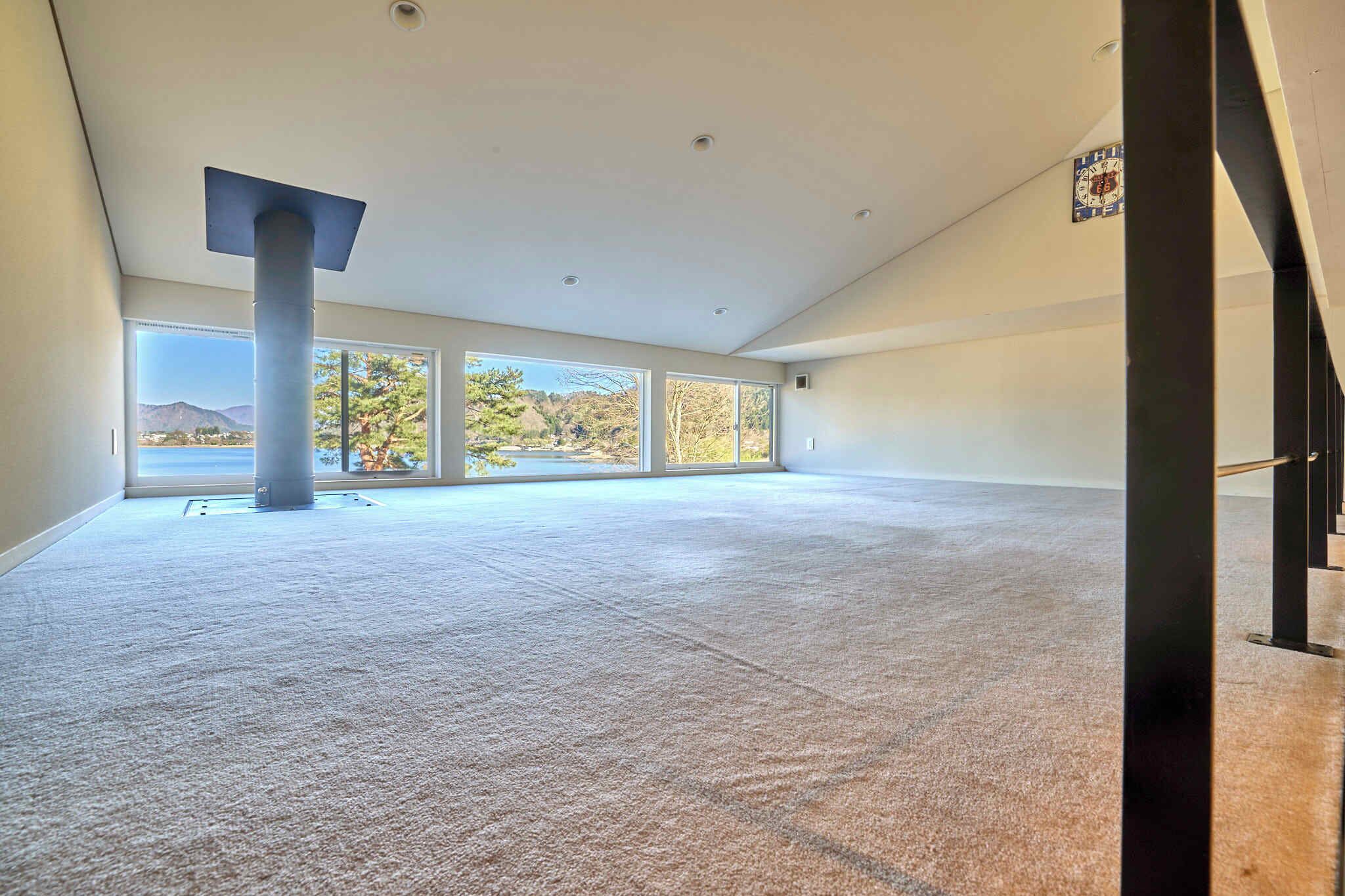 A spacious room with large windows, a central pillar, and a visible staircase.