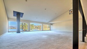 Una habitación amplia con ventanas grandes, un pilar central y una escalera a la vista.