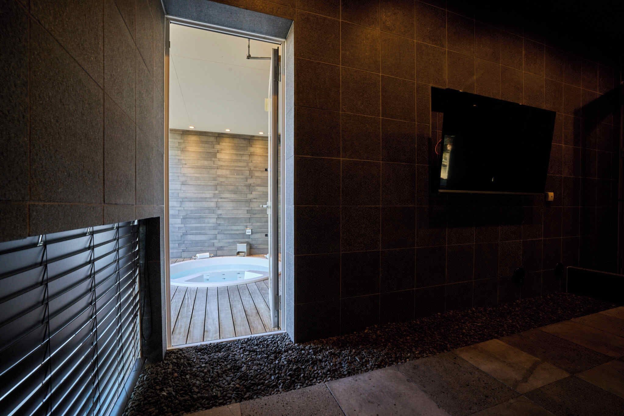 Un bagno moderno con una parete in pietra, un pavimento in legno e una vasca da bagno.